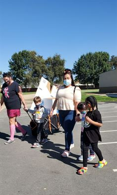 One adult walking with two children. One adult and child pulling a wagon with recycling in it.